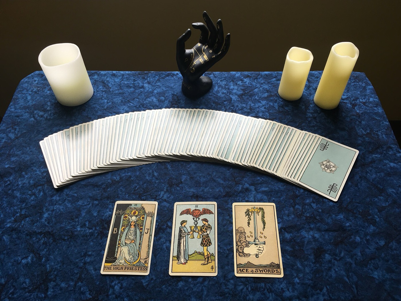 Cartas abertas em leque sobre pano azul, com velas ao lado